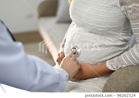 Female doctor using a stethoscope to listen to the baby's heartbeat in a pregnant woman's belly. 96262524