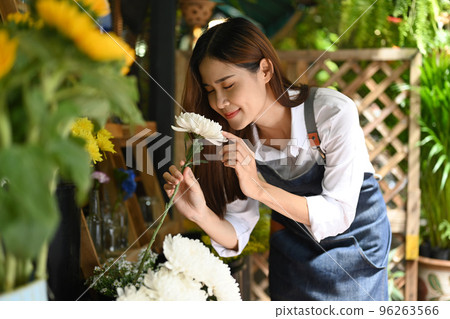 Beautiful female florist smelling white flowers with eyes closed. Business, sale and floristry concept 96263566