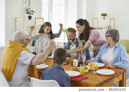 Happy joyful family sitting around table at home and having holiday meal all together Happy joyful family sitting around table at home and having holiday meal all together 96264242
