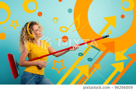 Girl with headset use the broom like a guitar. Cyan background 96266809
