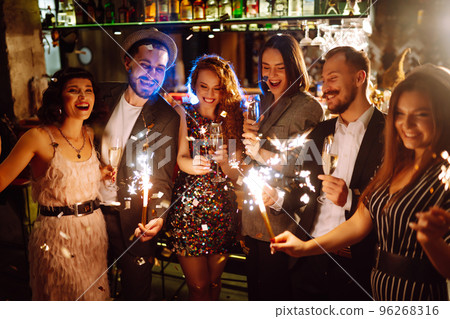 Glowing sparkles in hands. Group of happy people enjoying party with fireworks. Winter holiday. 96268316