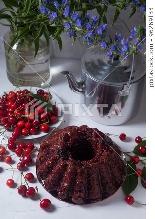Chocolate cake with sweet cherry, vintage kettle and bouquet of blue flowers on white background.. Chocolate cake with sweet cherry, vintage kettle and bouquet of blue flowers on white background.. 96269133