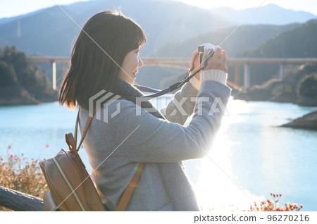 A woman taking a picture at the lakeside of the setting sun A woman taking a picture at the lakeside of the setting sun 96270216