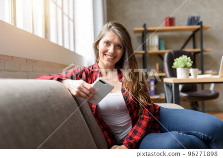 Smiling girl relaxing on a sofa with her smartphone Smiling girl relaxing on a sofa with her smartphone 96271898