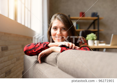 Smiling girl relaxing on a sofa with her smartphone 96271901