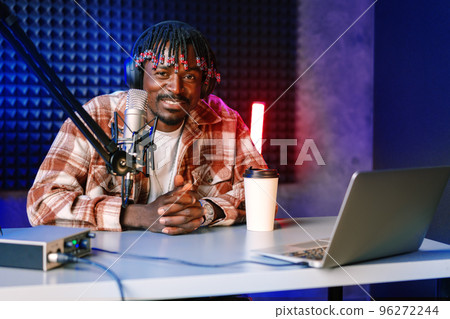 African radio host sitting at desk recording in studio with microphone and laptop African radio host sitting at desk recording in studio with microphone and laptop 96272244