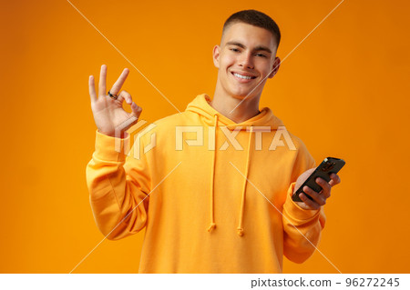 Portrait of a smiling young man holding mobile phone on yellow background Portrait of a smiling young man holding mobile phone on yellow background 96272245