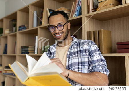 Arab male student reading book and learning while sitting in university library indoors, copy space Arab male student reading book and learning while sitting in university library indoors, copy space 96272565