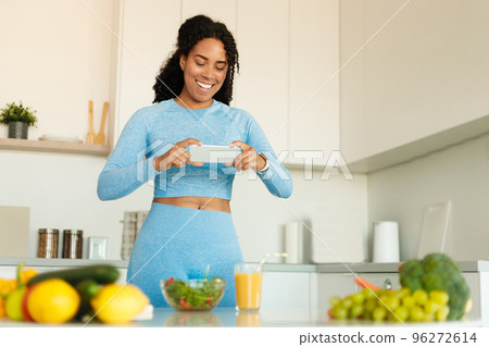 Food blogging concept. Black fitness blogger taking photo of healthy dinner on cellphone, cooking salad in kitchen 96272614