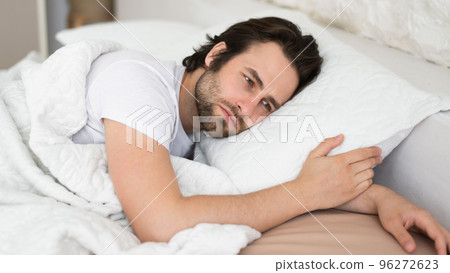 Tired sad depressed millennial caucasian man with stubble cant fall asleep in white bed, suffer from health problems Tired sad depressed millennial caucasian man with stubble cant fall asleep in white bed, suffer from health problems 96272623