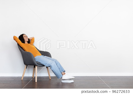Relaxed young woman reclining in arm chair over white wall Relaxed young woman reclining in arm chair over white wall 96272633
