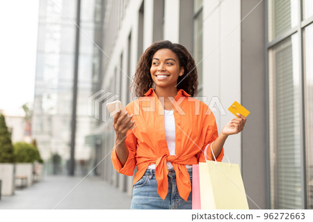 Glad happy millennial black lady in casual with smartphone, credit card and a lot of packages Glad happy millennial black lady in casual with smartphone, credit card and a lot of packages 96272663