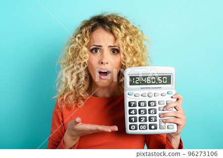 Girl is shocked and shows her debt on calculator display. Cyan background 96273106