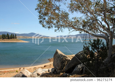 Jindabyne, New South Wales, Australia: View over Lake Jindabyne with a tree and rocks in the foreground. Jindabyne is a tourist destination near the Snowy Mountains. 96273274