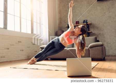 Young woman follows with a laptop a gym exercises. She is at home due to coronavirus codiv-19 quarantine 96273831