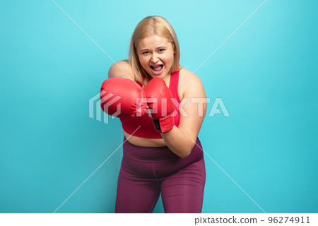 Fat girl in fitness suite does boxing. Cyan background 96274911