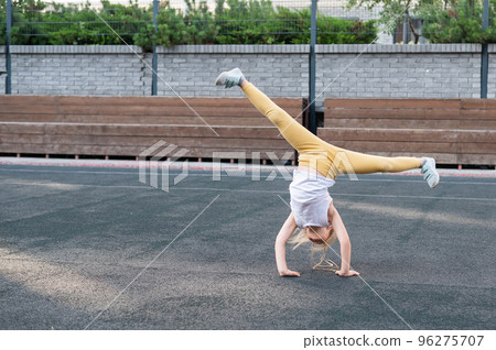 Caucasian girl makes a cartwheel on the sports field outdoors. Caucasian girl makes a cartwheel on the sports field outdoors. 96275707
