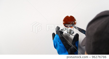 electrician installing light switch on painted wall with screwdriver. Man installing light switch after home renovation. 96276786