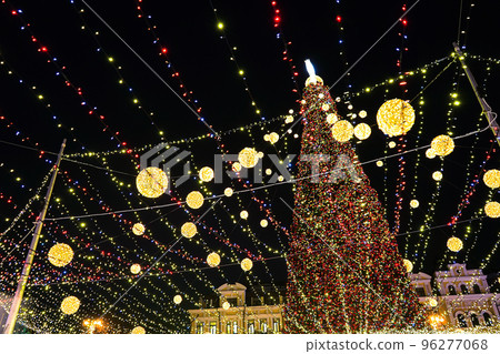 Christmas tree glows on the square in the city. Evening, night illumination Christmas tree glows on the square in the city. Evening, night illumination 96277068