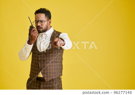 Frowning man speaking in walkie-talking and pointing at camera Frowning man speaking in walkie-talking and pointing at camera 96277148