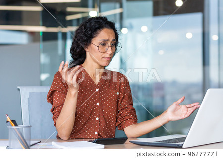 Businesswoman disappointed and sad at work, not happy with the result of achievement at work, Hispanic woman desperate and sad working inside office using laptop at work. Businesswoman disappointed and sad at work, not happy with the result of achievement at work, Hispanic woman desperate and sad working inside office using laptop at work. 96277771