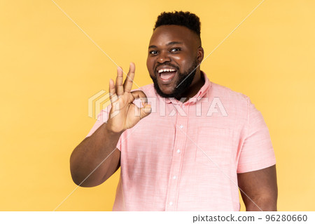 Ok sign, approval. Portrait of handsome man wearing pink shirt doing okay gesture and smiling with joyous satisfied contented expression. Indoor studio shot isolated on yellow background. Ok sign, approval. Portrait of handsome man wearing pink shirt doing okay gesture and smiling with joyous satisfied contented expression. Indoor studio shot isolated on yellow background. 96280660