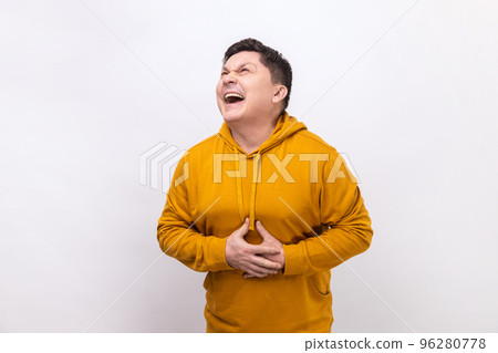 Portrait of extremely excited happy man holding his belly and laughing out loud, chuckling giggling at amusing joke, wearing urban style hoodie. Indoor studio shot isolated on white background. 96280778