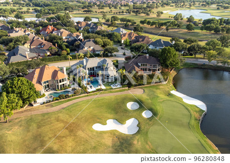 Aerial overview of luxury villas with swimming pools located around green zone, lake and golf playground in the summertime. 96280848