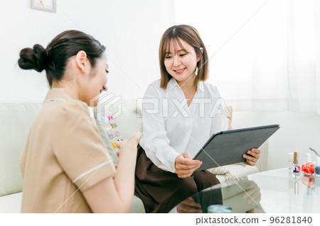 一位美甲師在美甲沙龍解釋計劃和設計,一位日本女性一邊看樣品一邊在平板電腦上進行選擇 一位美甲師在美甲沙龍解釋計劃和設計,一位日本女性一邊看樣品一邊在平板電腦上進行選擇 96281840