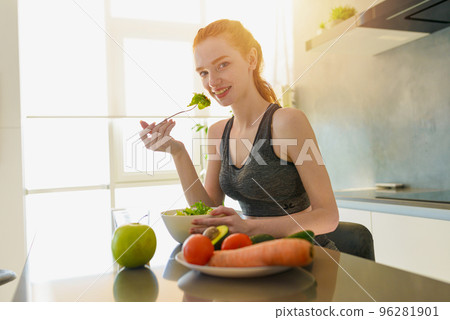Athletic girl with gym clothes eats salad in the kitchen 96281901