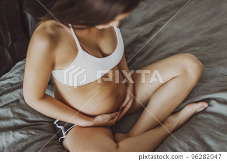 Pregnant woman sitting in bed during pregnancy holding stomach during first trimester. Woman thinking about her baby and motherhood. Happy multiracial model showing belly. Maternity, health concept. 96282047