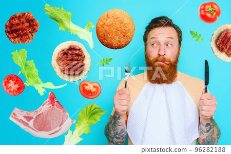 Man with tattoos is ready to eat with cutlery in hand. cyan background 96282188