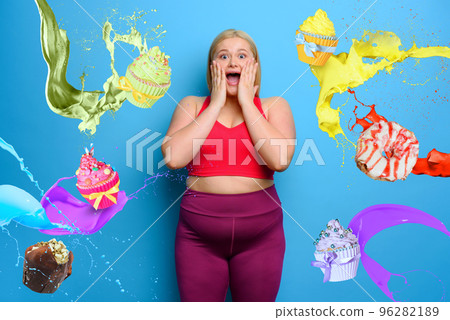 Fat woman with shocked and surprised expression because she is surrounded by sweets. Cyan background 96282189