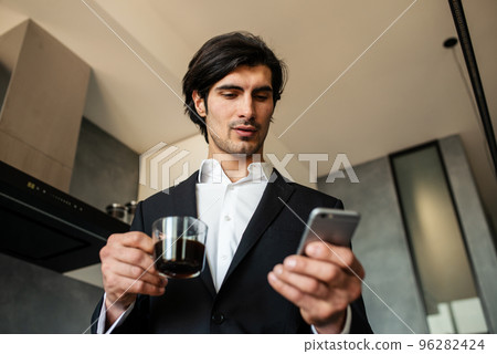 Businessman read news from smartphone while drinking a coffee at home Businessman read news from smartphone while drinking a coffee at home 96282424