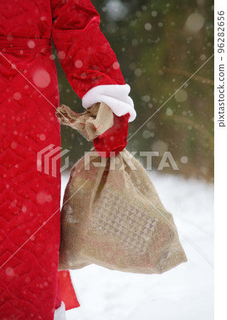 Santa Claus with bag of Christmas gifts is walking through snowy forest. Animator or parent in Santa Claus costume is rushing to a holiday for children. Traditions of winter holidays Santa Claus with bag of Christmas gifts is walking through snowy forest. Animator or parent in Santa Claus costume is rushing to a holiday for children. Traditions of winter holidays 96282656
