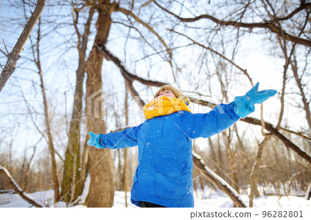 Little boy throwing fresh snow from his hands. Child enjoy walking in the park on snowy day. Baby having fun during snowfall. Outdoor winter activities for kids. 96282801