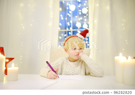 Little spoilit boy writing the letter to Santa. Wayward child think of a gift that he can receive. Traditions around New Year and Christmas Holidays. Little spoilit boy writing the letter to Santa. Wayward child think of a gift that he can receive. Traditions around New Year and Christmas Holidays. 96282820