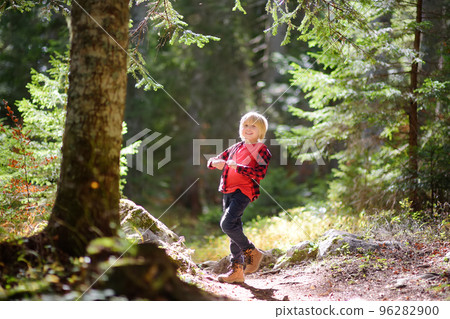 Cheerful school child is hiking and exploring nature in the forest. Little boy travel in the sunny woodland. Summer vacation activity for kids in forest. 96282900