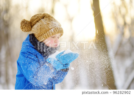Little boy blowing snow from his hands. Child enjoy walking in the park on snowy day. Baby having fun during snowfall. Outdoor winter activities for kids. Little boy blowing snow from his hands. Child enjoy walking in the park on snowy day. Baby having fun during snowfall. Outdoor winter activities for kids. 96282902