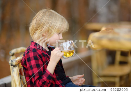 Little boy drinking a herbal fragrant tea in a rural cafe with wooden furniture. Tea is a traditional hot drink in many countries. Little boy drinking a herbal fragrant tea in a rural cafe with wooden furniture. Tea is a traditional hot drink in many countries. 96282903