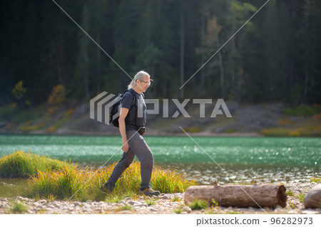 Gray haired mature man traveling in the National Park Durmitor, Montenegro. Senior tourist hiking near mountain lake. Solo journey. Backpacking hike Gray haired mature man traveling in the National Park Durmitor, Montenegro. Senior tourist hiking near mountain lake. Solo journey. Backpacking hike 96282973