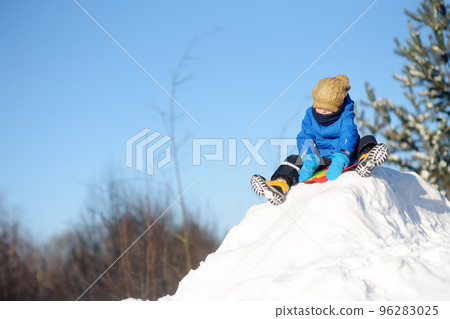 Little boy enjoy riding on ice slide on snowy day. Baby having fun during blizzard. Outdoor winter activities for kids. 96283025