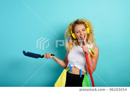 Funny housewife use broom like a rock microphone. cyan background Funny housewife use broom like a rock microphone. cyan background 96283054