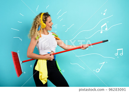 Funny housewife use broom like a rock guitar. cyan background 96283091
