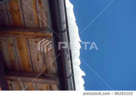 The roof of a house on a snowy winter day among thaw. Cleaning the roofing from snow and icicles. The roof of a house on a snowy winter day among thaw. Cleaning the roofing from snow and icicles. 96283103