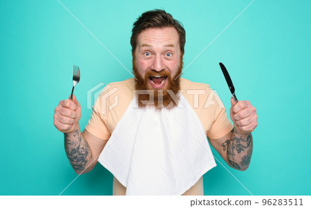 Man with tattoos is ready to eat with cutlery in hand. cyan background 96283511