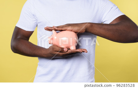 Man protects his piggy bank. concept of savings. yellow background Man protects his piggy bank. concept of savings. yellow background 96283528