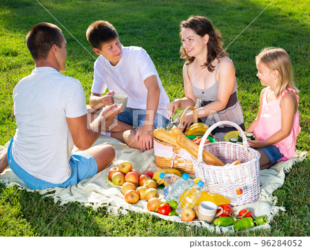 Cheerful woman picnicking with children and husband Cheerful woman picnicking with children and husband 96284052