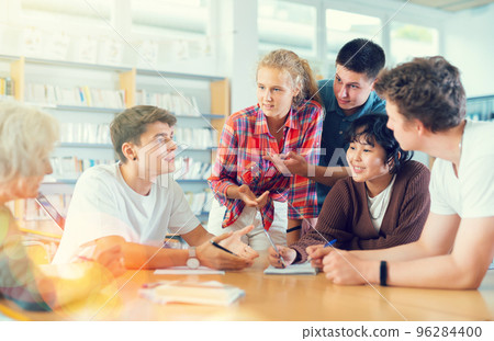 Positive teenage students working and discussing in groups in library Positive teenage students working and discussing in groups in library 96284400