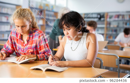 Two schoolgirls preparing for lesson with books in school library Two schoolgirls preparing for lesson with books in school library 96284436